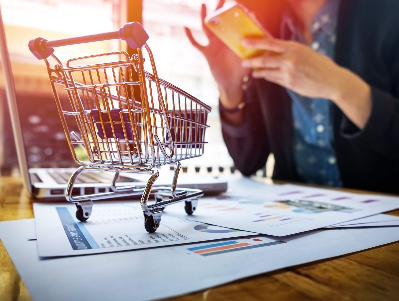 Carrinho de compras sobre relatórios financeiros, representando a análise de dados de um e-commerce