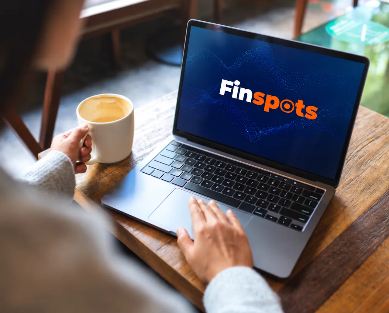 Pessoa tomando café em frente a um notebook com a marca Finspots na tela